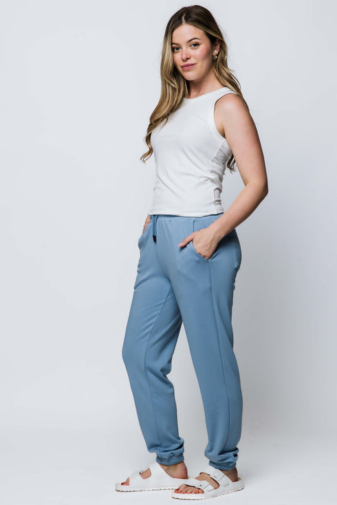 Woman wearing a white sleeveless top and blue pants on a white background