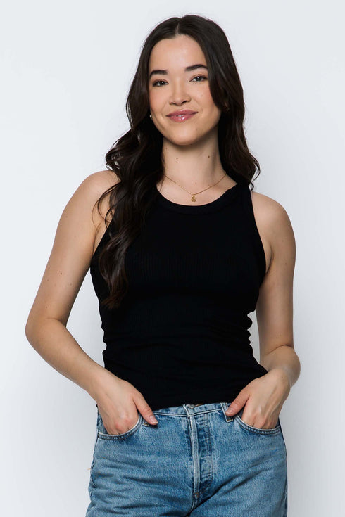 Woman wearing a black tank top and blue jeans against a white background