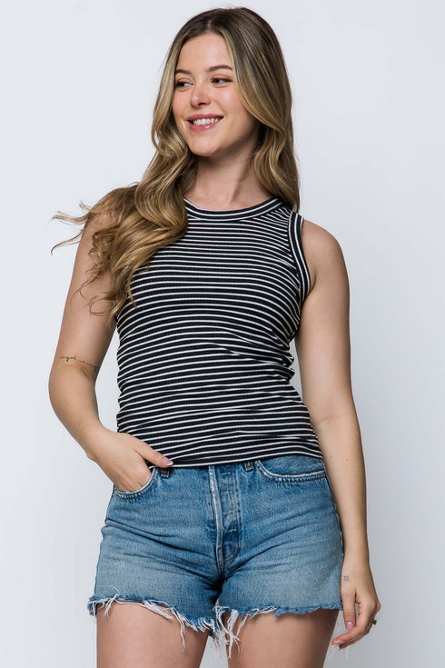 Woman wearing a black and white striped tank top and denim shorts on a plain background