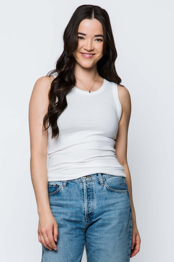 Woman wearing a white tank top and blue jeans against a plain background