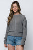 Woman wearing a gray sweater with a textured pattern and denim shorts on a white background