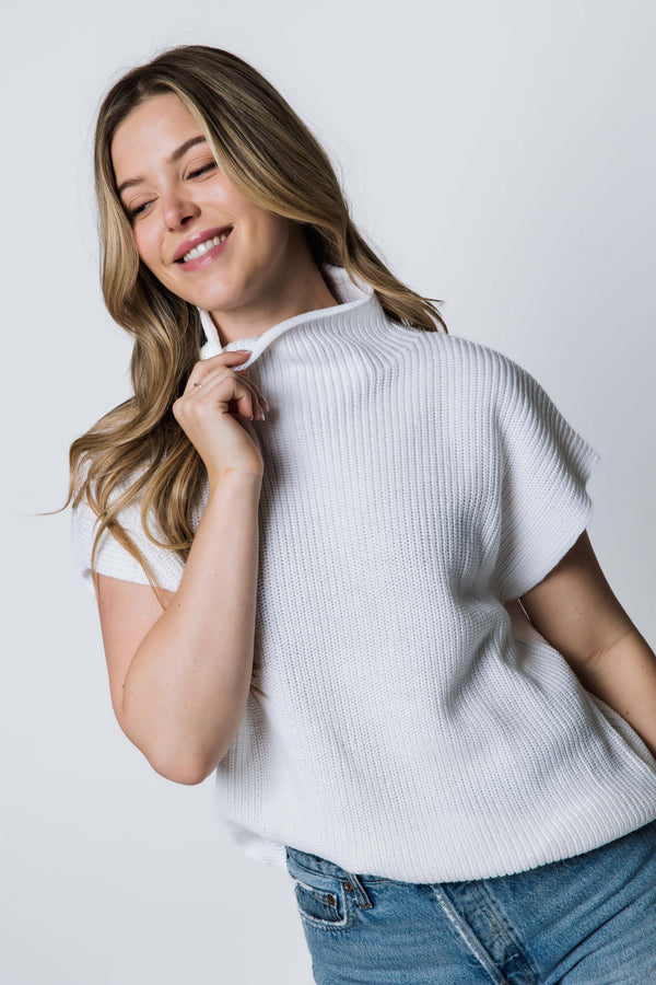 Woman wearing a white short-sleeve sweater against a plain background