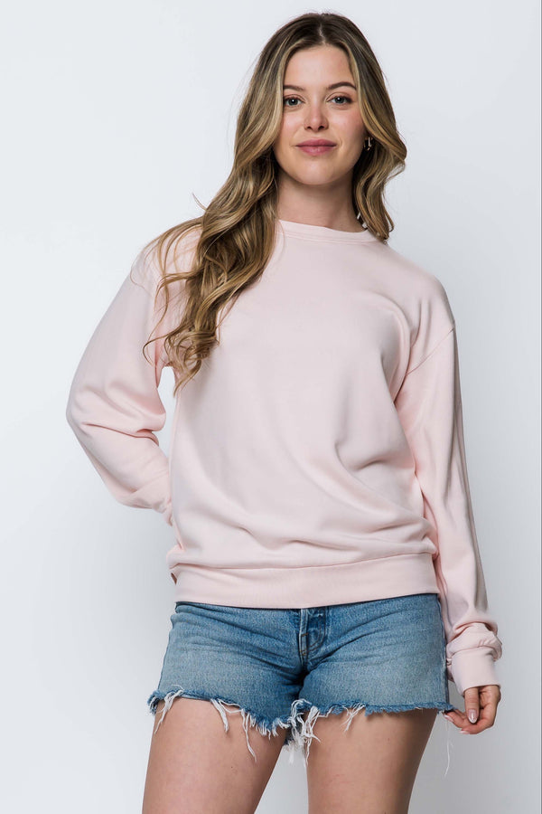 Woman wearing a light pink sweater and denim shorts on a white background