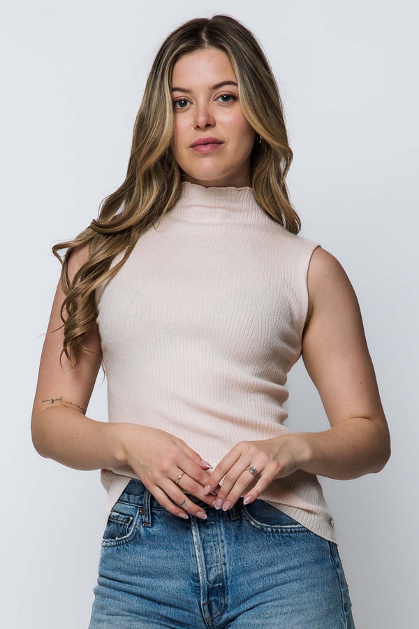 Woman wearing a light pink sleeveless top and blue jeans against a white background