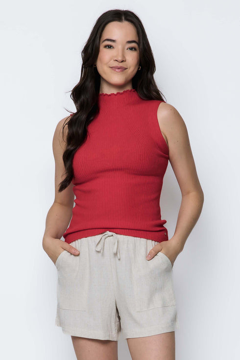Woman wearing a red sleeveless top and beige shorts against a white background