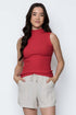 Woman wearing a red sleeveless top and beige shorts against a white background