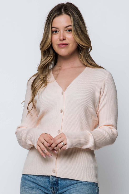 Woman wearing a light pink cardigan over a white shirt with blue jeans on a plain background