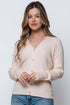 Woman wearing a light pink cardigan over a white shirt with blue jeans on a plain background