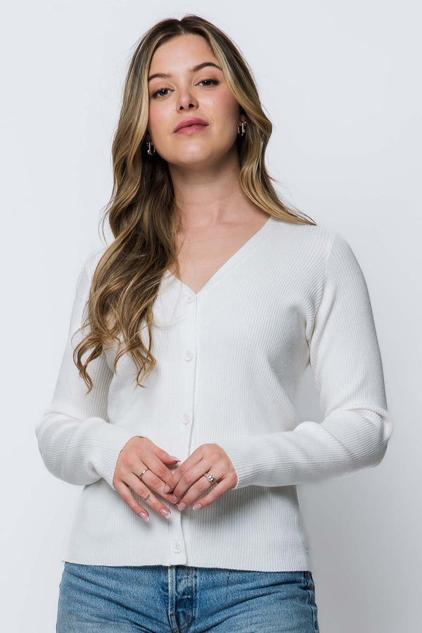 Woman wearing a white cardigan over a blue top against a plain background