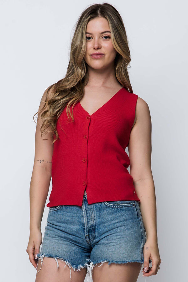 Woman wearing a red sleeveless top and denim shorts against a white background