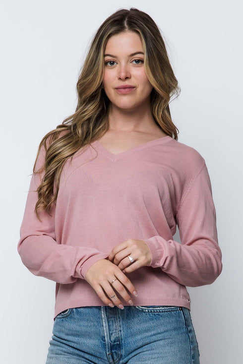 Woman wearing a pink long-sleeve top and blue jeans against a white background