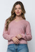 Woman wearing a pink long-sleeve top and blue jeans against a white background