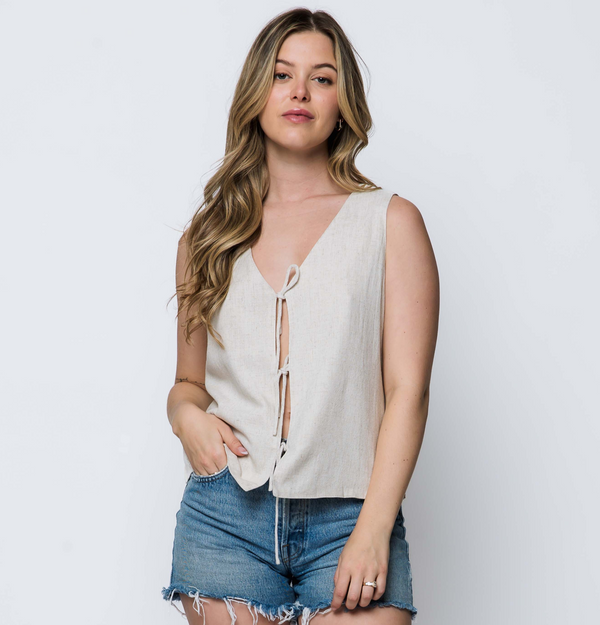 Woman wearing a sleeveless beige top and denim shorts on a plain background